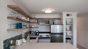A modern kitchen with white countertops, stainless steel appliances, and wooden shelves.