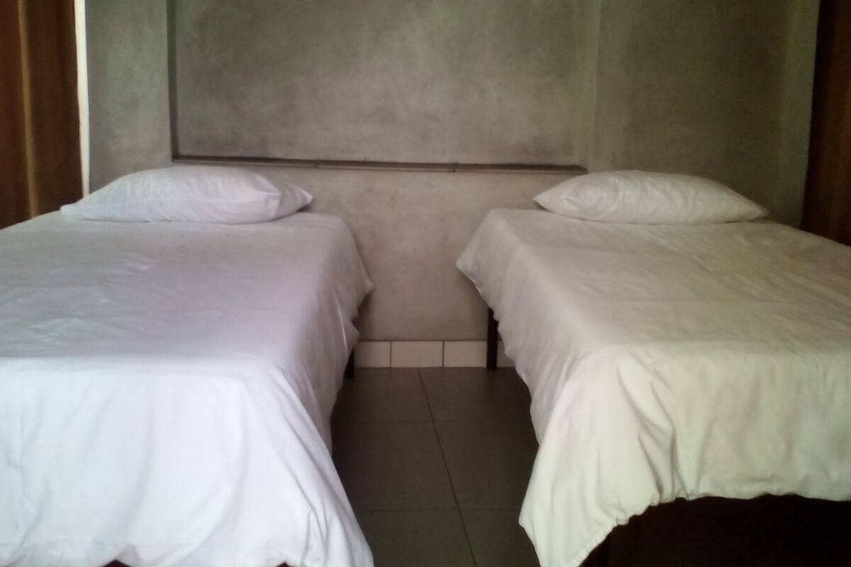 Ein Zimmer mit zwei Einzelbetten, Fliesenboden und einer schlichten Wand.
