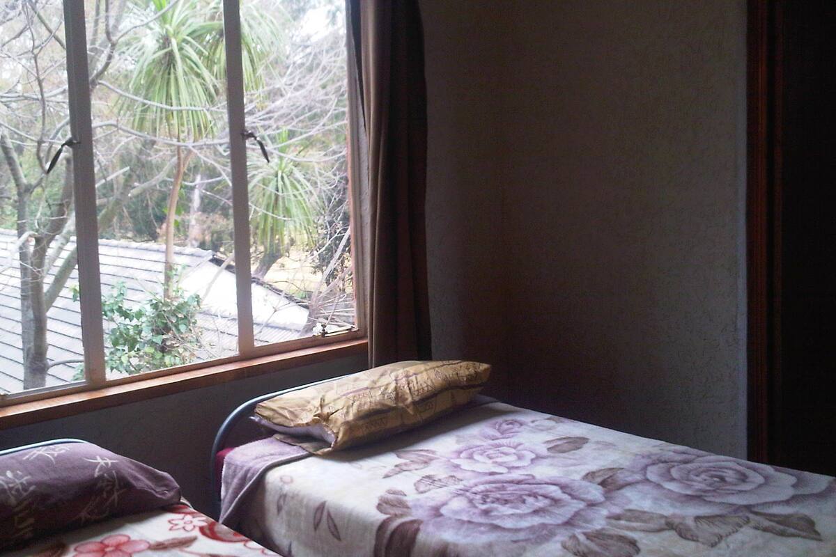 Ein Schlafzimmer mit einem Einzelbett, einem Fenster mit Blick auf Bäume und einem Vorhang.
