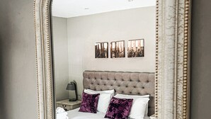 A bedroom with a large mirror, a tufted headboard, a bed with white linens and purple pillows, and three framed pictures on the wall. - Rising Sun Hotel (Lynmouth)