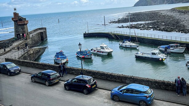 A coastal road with parked cars, a stone pier with boats, and a lighthouse. - Rising Sun Hotel (Lynmouth)