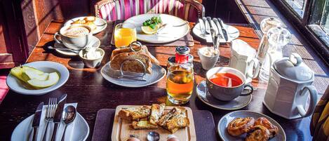 Una mesa de desayuno dispuesta con tostadas, huevos y bollería, junto con tazas de café y té.