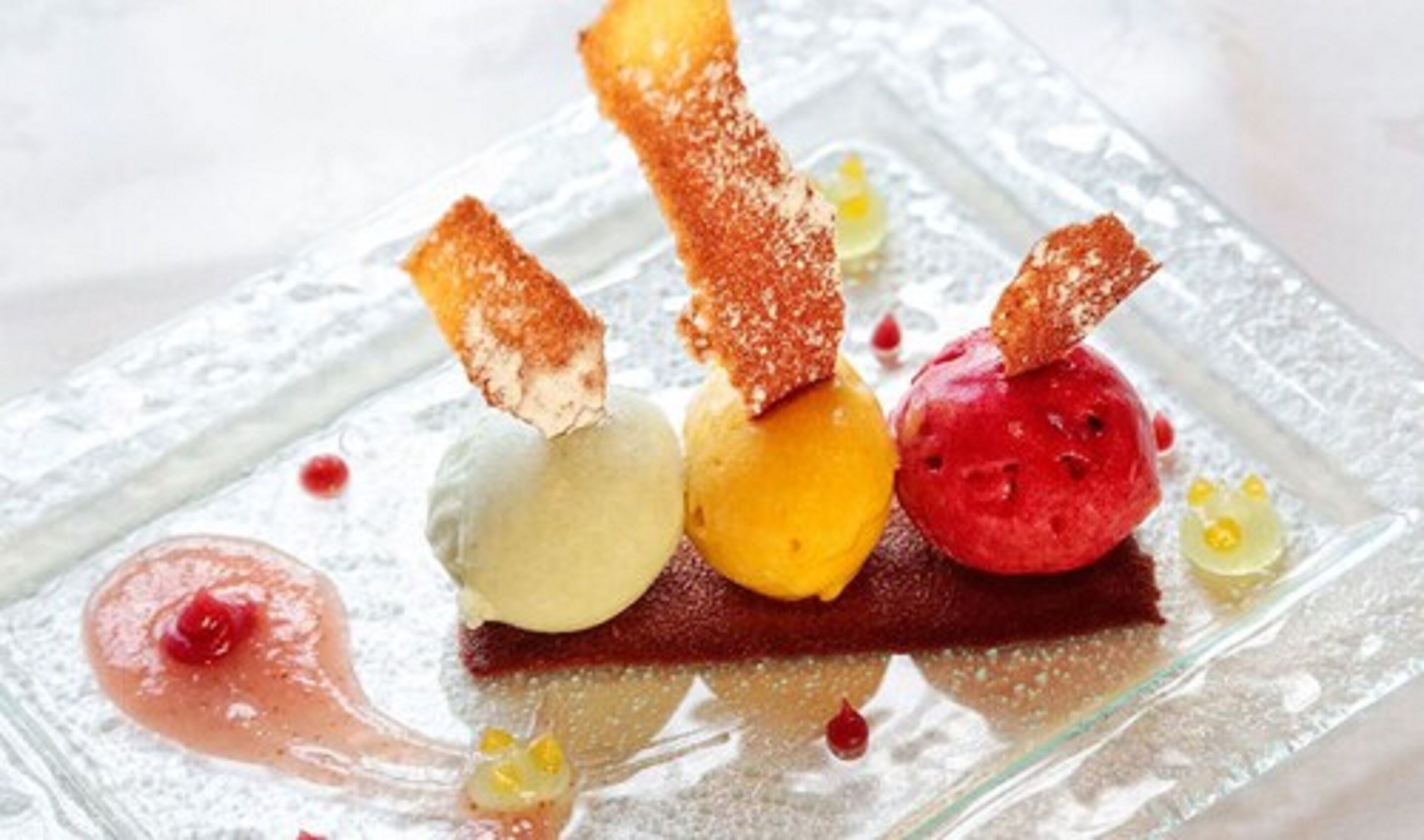 A dessert plate with various ice cream flavors and a chocolate piece.