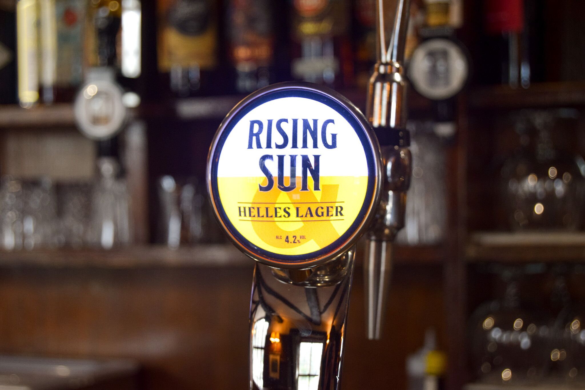 A beer tap labeled "RISING SUN Helles Lager" with a 4.2% alcohol by volume.