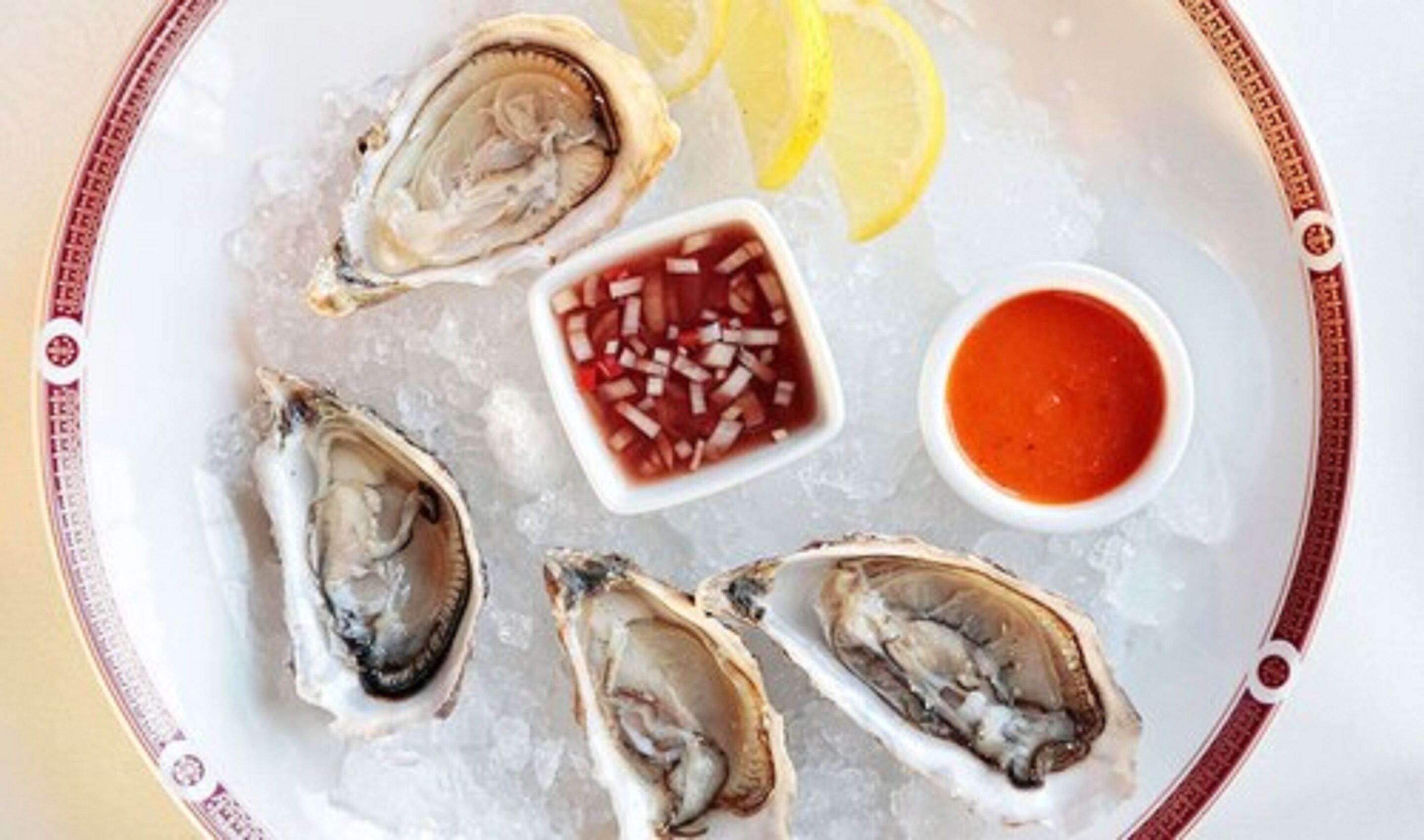 A plate with oysters, lemon wedges, and two types of sauces.