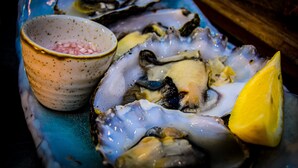 A plate of oysters with a lemon wedge and a small bowl of pickles.