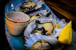 A plate of oysters with a lemon wedge and a small bowl of pickles.