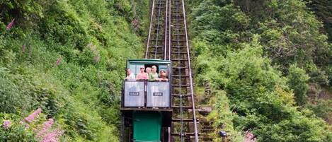 A cable car ascending a steep, narrow railway track surrounded by lush greenery.