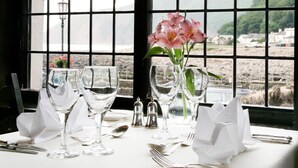 A table set for dining with a view of a coastal landscape through a window with a grid pattern. - Rising Sun Hotel (Lynmouth)