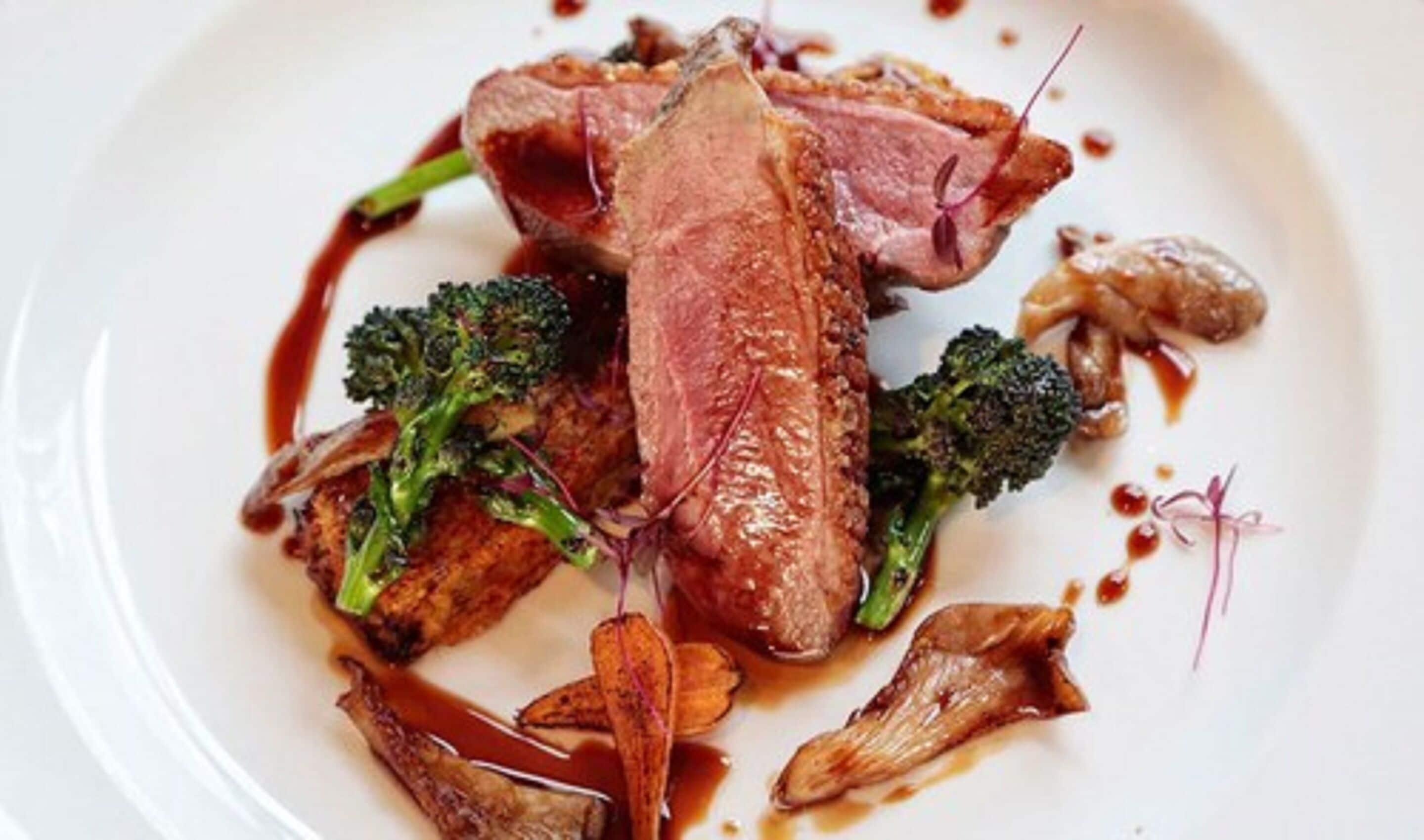 Un plato de comida con pato, brócoli y champiñones.