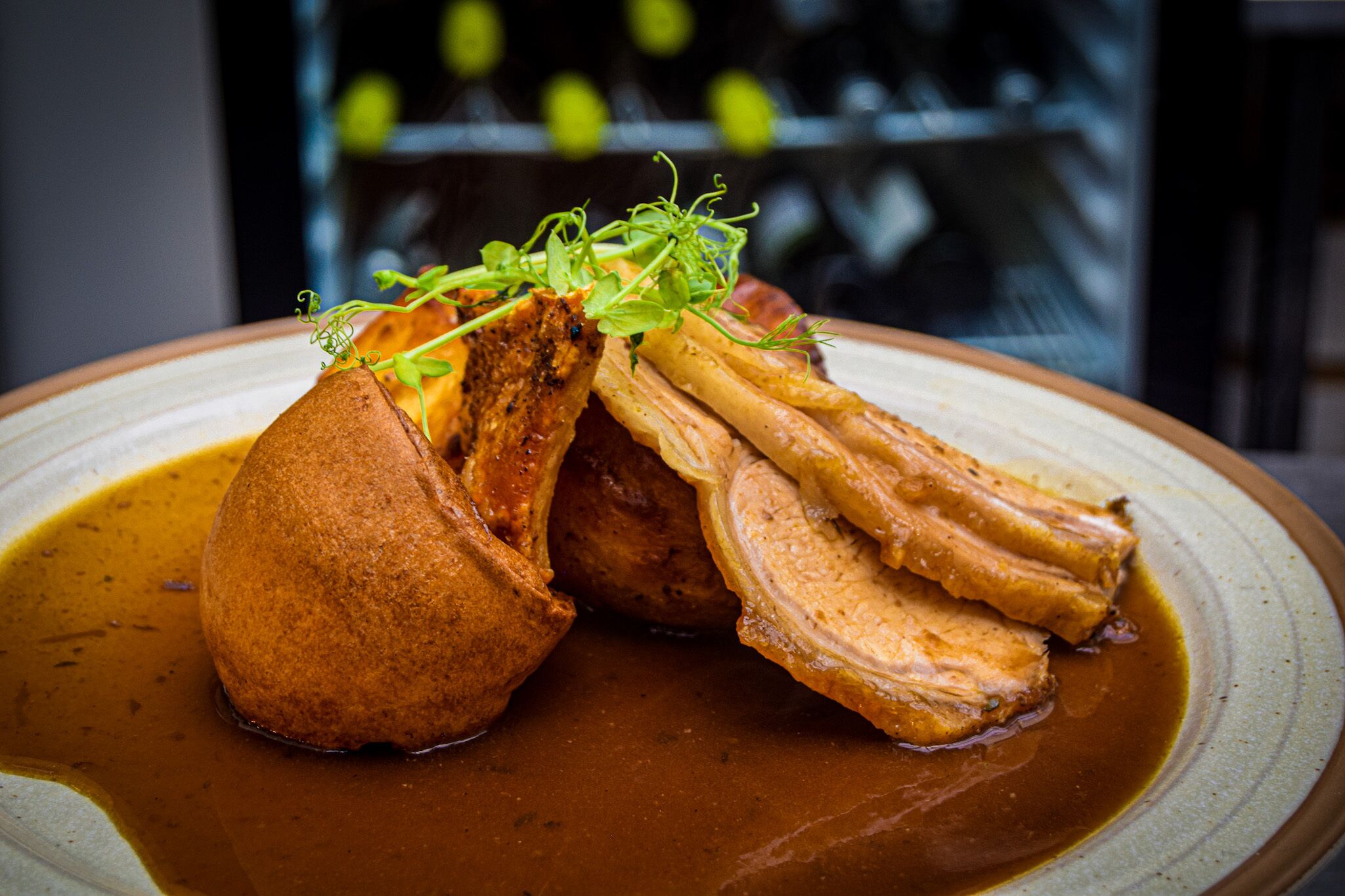 A dish with a roasted item, possibly pork, served with a sauce and garnished with green herbs.