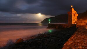 A stone tower by the sea at night with a cloudy sky.