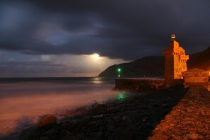 A stone tower by the sea at night with a cloudy sky.
