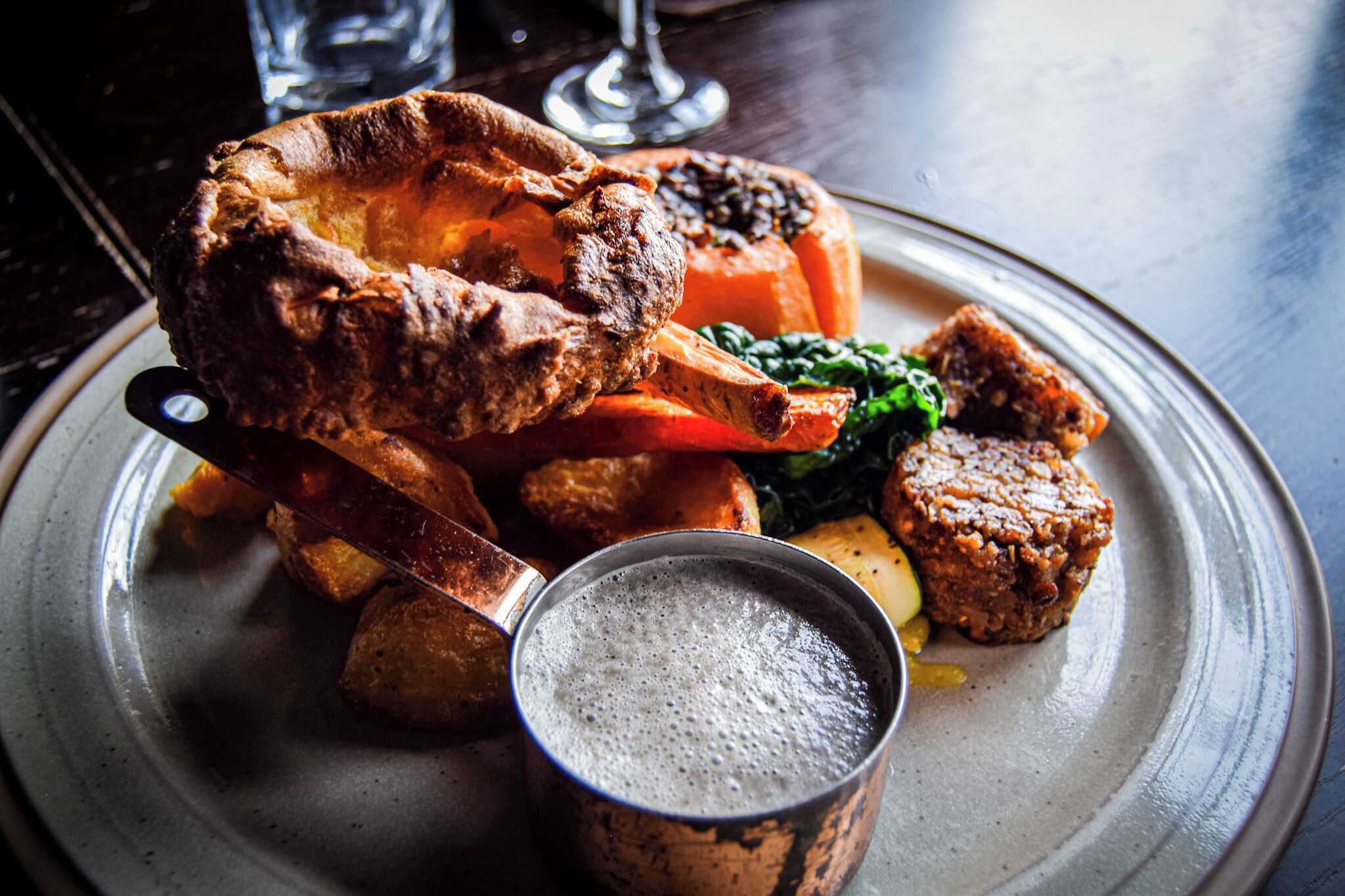 Un piatto di cibo con pudding dello Yorkshire, carne arrosto, verdure e un piccolo bicchiere di salsa gravy.
