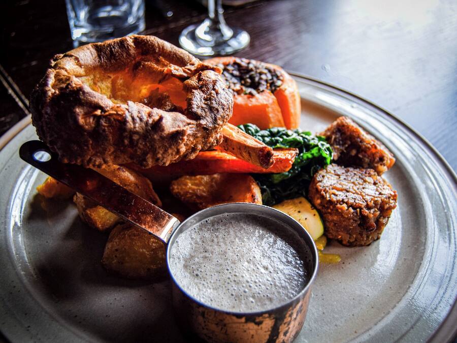 A plate of food including a Yorkshire pudding, roasted meat, vegetables, and a small cup of gravy.