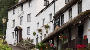 A white building with a signboard advertising The Rising Sun Hotel, offering fresh local produce, a variety of meats, seafood, locally supplied vegetables, and homemade bread. - Rising Sun Hotel (Lynmouth)