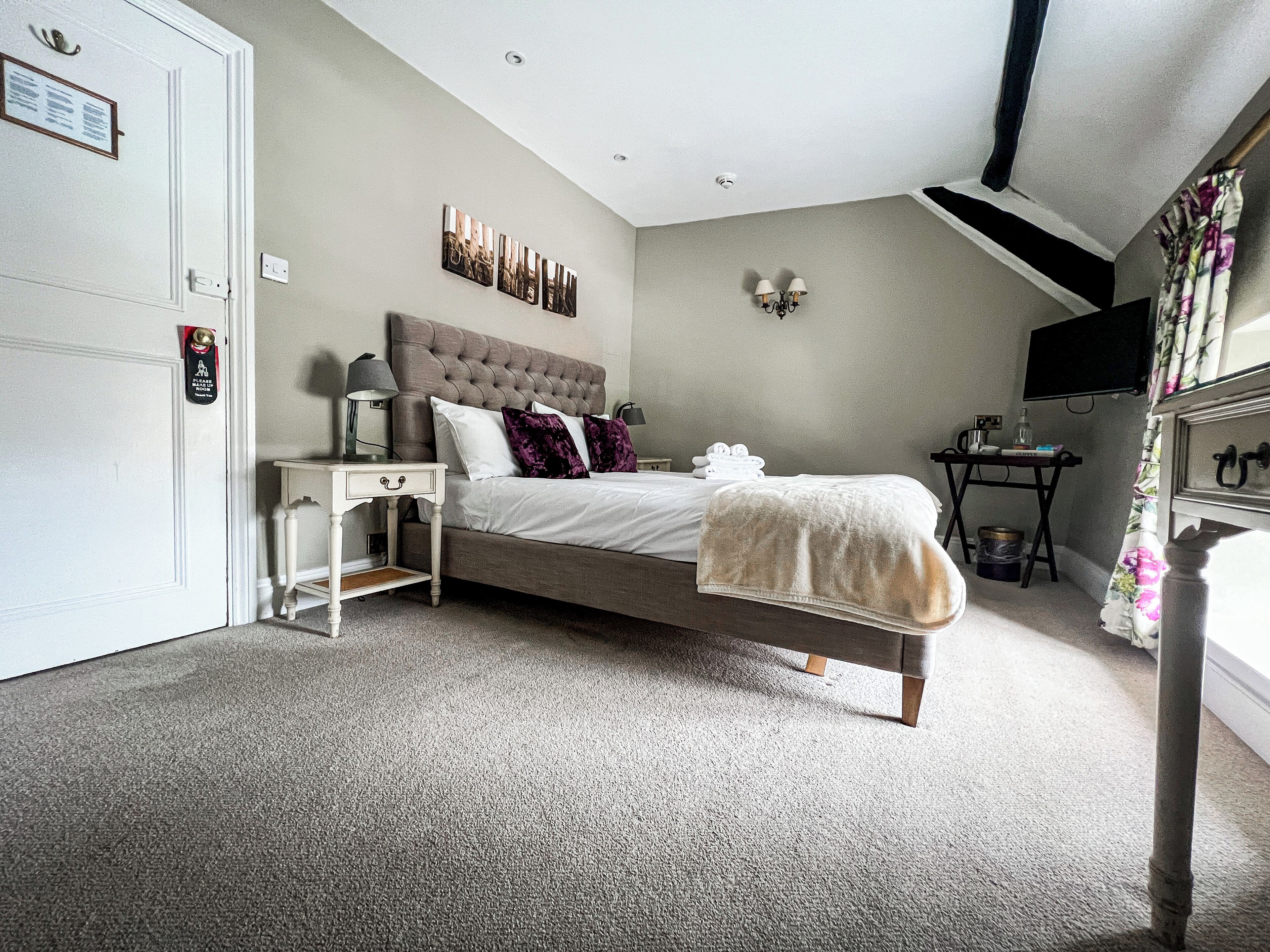 A bedroom with a bed, bedside table, lamp, wall art, and a television.