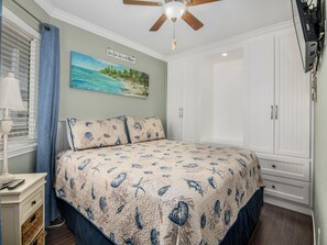 A bedroom with a bed, a ceiling fan, a painting, and a wardrobe.