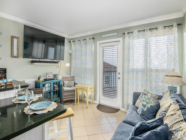 A cozy living room with a sofa, a TV mounted on the wall, and a dining area with a table and chairs.