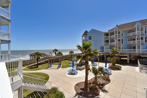 A beachfront hotel with a patio area, outdoor seating, and a view of the ocean.