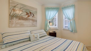 Une chambre à coucher avec une couvre-lit à rayures, un tableau au mur et une fenêtre avec des rideaux.