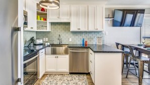A modern kitchen with white cabinets, stainless steel appliances, and a black countertop. - Seascape 2317 Studio Bedroom Condo by RedAwning (Galveston)