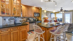 A kitchen with wooden cabinets, a microwave, and a dining area with wicker chairs. - Seascape 1209 2 Bedroom Condo by RedAwning (Galveston)