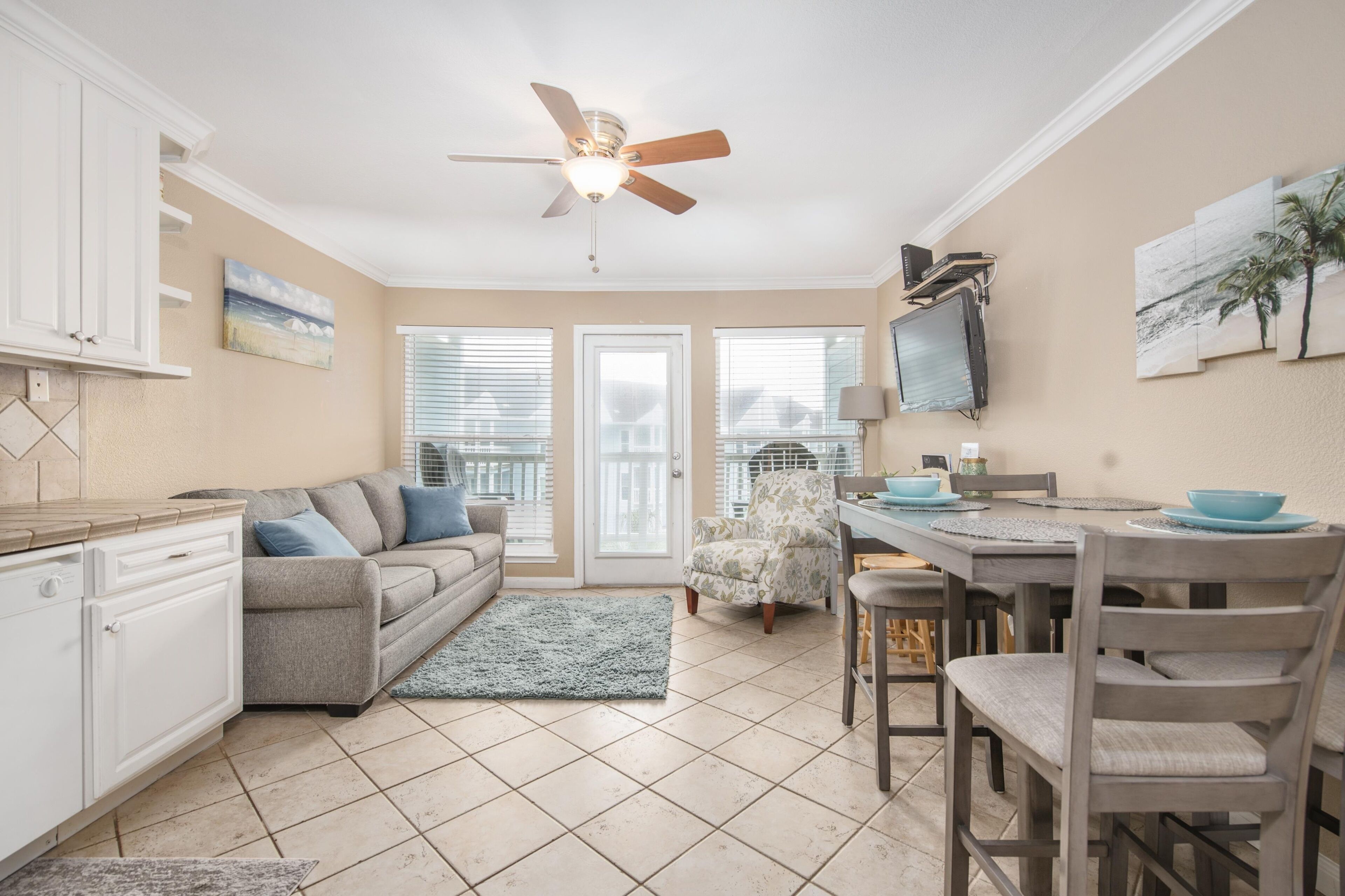 A kitchen with a ceiling fan, a dining area with a table and chairs, and a gray sofa.