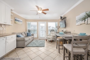 A kitchen with a ceiling fan, a dining area with a table and chairs, and a gray sofa.
