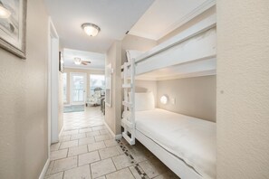 Un couloir avec des lits superposés, un ventilateur de plafond et une vue sur un espace de vie.