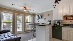 A kitchen with a central island, white cabinetry, a ceiling fan, and a view through glass doors to the outside. - Seascape 2105 1 Bedroom Condo by RedAwning (Galveston)