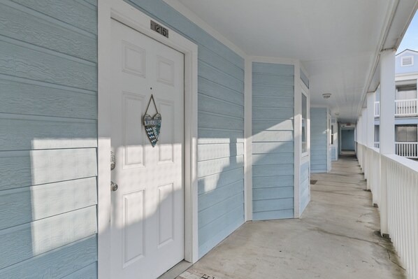 A corridor with light blue siding and white trim, leading to a door marked with the number 1215.