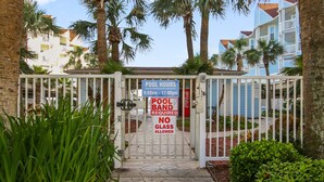 A gated pool area with a sign indicating pool hours from 9:00am to 11:00pm, a pool band requirement, and a no glass allowed policy. - Seascape 2201 2 Bedroom Condo by RedAwning (Galveston)