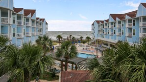 A beachfront hotel with multiple-story buildings, a swimming pool, and palm trees. - Seascape 2201 2 Bedroom Condo by RedAwning (Galveston)