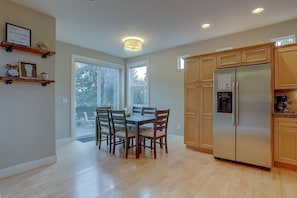 A modern kitchen with wooden cabinets, a stainless steel refrigerator, and a dining table with chairs. - Vantage Point 3 Bedroom Townhouse by RedAwning (Bend)