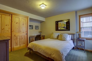 Un dormitorio con cama, armario de madera, escritorio, silla y una obra de arte en la pared.