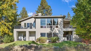A modern two-story house with a balcony, large windows, and a well-maintained lawn.