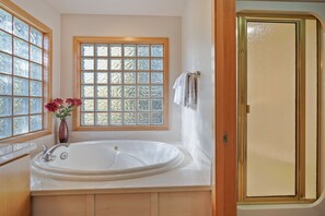 A bathroom with a large bathtub, a window with frosted glass, and a wooden door.