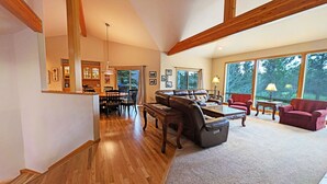 A spacious living room with a wooden floor, a leather sofa, a coffee table, and a dining area with a wooden table and chairs.
