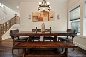 A dining area with a large wooden table, six chairs, a chandelier, and a decorative wall piece. - Trails End 5 Bedroom Home by RedAwning (Bend)