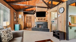 A cozy living room with a fireplace, a sofa, a coffee table, and a television mounted on the wall. - 7 Grizzly Home New Private Hot Tub on the Deck and Bike for Adventure by RedAwning (Bend)