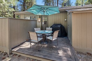 A deck with a table and chairs, an umbrella, and a grill.
