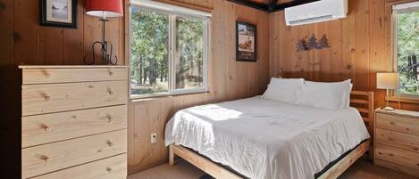 A wooden-paneled bedroom with a bed, dresser, and window.