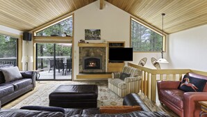 A spacious living room with a fireplace, leather sofas, and large windows. - 2 Quail Home Private Hot Tub, Steps from SHARC and short walk to the Sunriver Village by RedAwning (Bend)