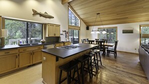A spacious kitchen with wooden cabinets, a large island with bar stools, and a dining area with a table and chairs. - 2 Quail Home Private Hot Tub, Steps from SHARC and short walk to the Sunriver Village by RedAwning (Bend)