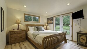 A bedroom with a wooden bed, a nightstand, a dresser, a television, and a window with a view of greenery. - 2 Quail Home Private Hot Tub, Steps from SHARC and short walk to the Sunriver Village by RedAwning (Bend)