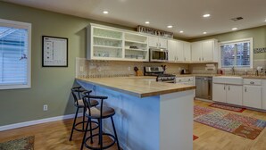 A kitchen with a central island, bar stools, white cabinets, a microwave, and a food & wine chart on the wall.