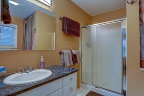 A bathroom with a white sink, a mirror, a shower with a glass door, and towels hanging on the wall.