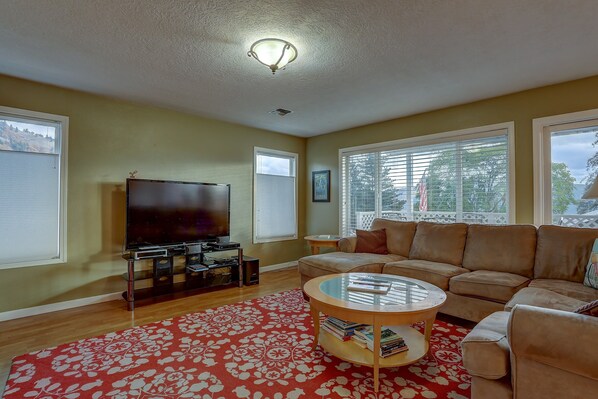 A living room with a large flat-screen TV, a beige sectional sofa, a red floral rug, and a round coffee table.