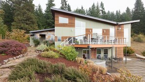 A modern two-story house with a balcony, surrounded by landscaped gardens and tall trees. - Mountain House 4 Bedroom Home by RedAwning (Parkdale)